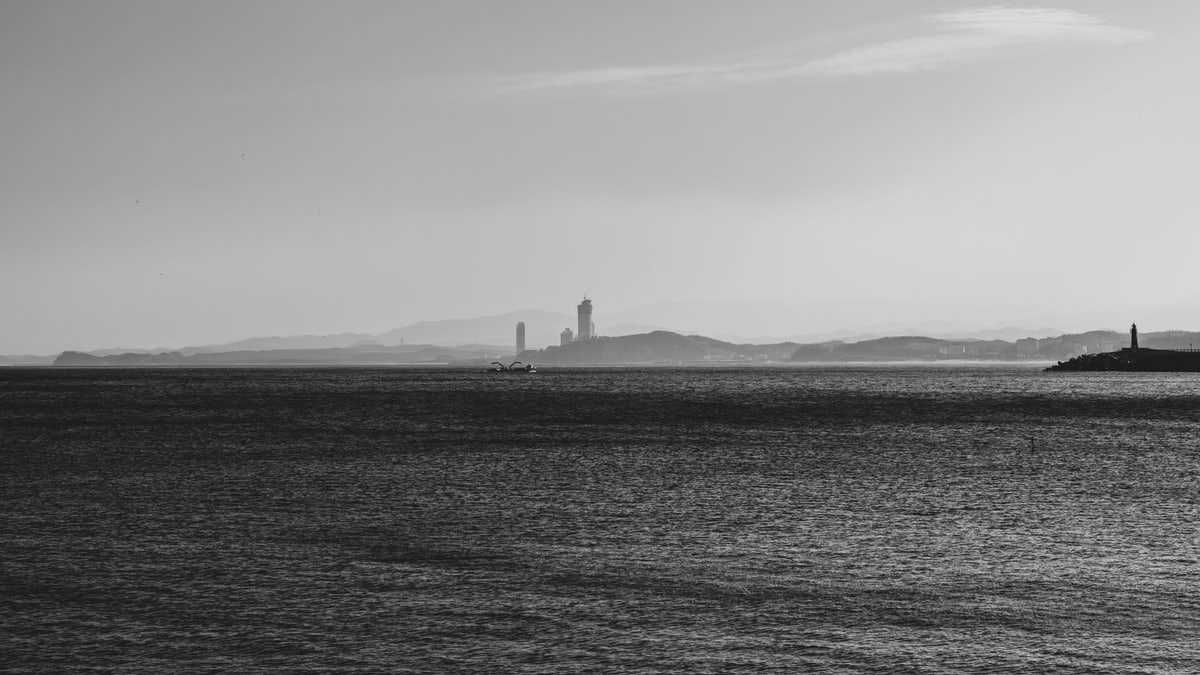 A serene black and white seascape featuring distant lighthouses and mountains, captured during the day.